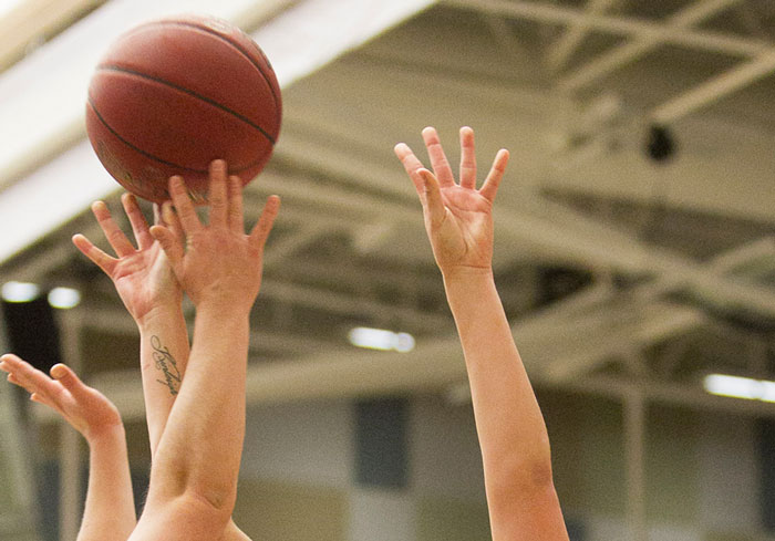 Zoomed in image of a basketball game with hands reaching for the ball